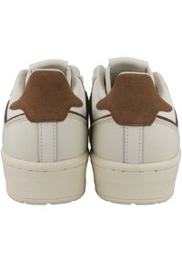 Białe sneakersy z brązowymi akcentami z zamszu, teksturowaną skórą, płaską gumową podeszwą oraz haftem na pięcie i bokach.