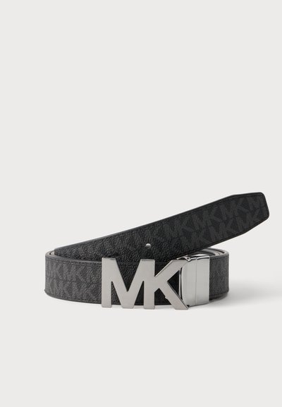 Ceinture en cuir noire avec motif répété "MK" et grande boucle en argent "MK" posée à plat sur fond blanc.