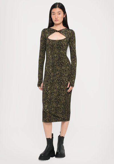 Robe longue à manches longues imprimée léopard avec une découpe en trou de serrure, dans des tons verts et noirs, associée à des bottes noires à semelle épaisse.