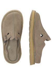 Beige suede slip-on shoes with a rounded toe and leather strap featuring a metal buckle. Rubber sole with a textured tread.