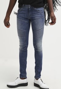 Jeans de mezclilla ajustados en azul lavado, con costuras en panel, acentos acanalados en los muslos y una cintura de media altura. Combinados con zapatos blancos.