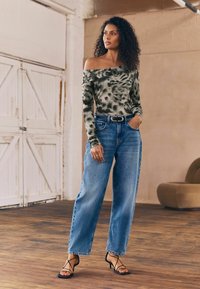 Off-the-shoulder tie-dye top i grå og grøn, parret med højtaljede blå jeans. Sorte strophæle fuldender outfittet.