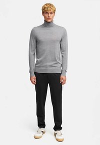 Szary sweter z golfem wykonany z delikatnego dzianinowego materiału, zestawiony z czarnymi spodniami i białymi trampkami z jasnobrązowymi akcentami.