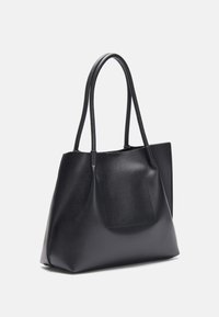 Sort læder tote bag med to lange stropper, trapezformet og en frontlomme. Glat tekstur med minimal hardware og detaljer.