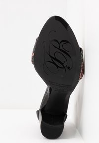 Semelle d'une chaussure noire pointue avec une écriture décorative et un texte, montrant un petit talon bloc et une pointe de talon texturée.