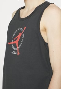 Svart ärmlös linne i bomull med en röd tryckt logotyp och text på framsidan, rundad halsringning och råa sömmar.