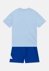 T-shirt di cotone azzurro con maniche corte e scollo rotondo, abbinata a pantaloni corti blu con un accento triangolare bianco vicino all'orlo.