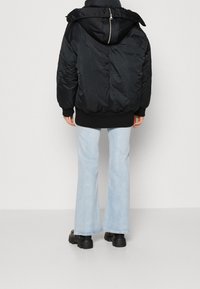 Chaqueta acolchada negra con capucha, con cierre de cremallera y puños acanalados, llevada sobre unos jeans flare de color azul claro y botas negras gruesas.