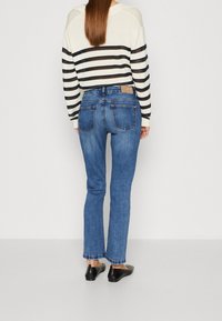 Lätt, randig tröja i krämfärg och svart. Tajt blå denimjeans med lätt utsvängning och midjehöjd. Svarta platta skor.