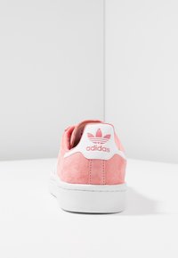 Sneaker in suede rosa con suola in gomma bianca, dotata di linguetta bianca sul tallone e logo adidas. La vista posteriore evidenzia la texture e i dettagli di design.