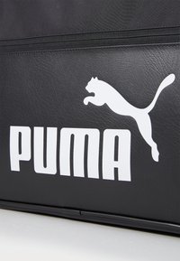 Borsa nera realizzata in materiale simile alla pelle, caratterizzata da un grande logo Puma bianco e da una scritta audace. Il design include una texture liscia e dettagli con cerniera.