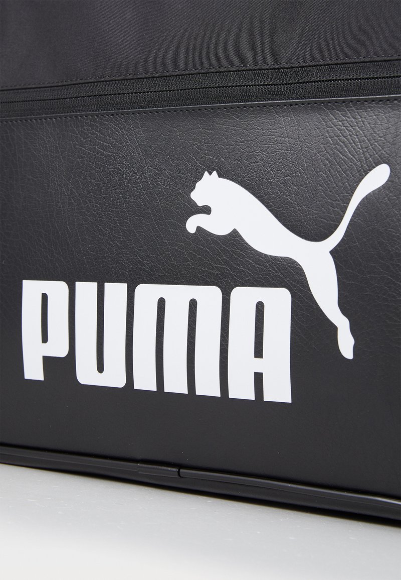 Borsa nera realizzata in materiale simile alla pelle, caratterizzata da un grande logo Puma bianco e da una scritta audace. Il design include una texture liscia e dettagli con cerniera.