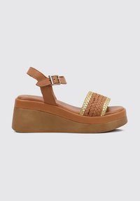 Wedge sandal in brown faux leather with a woven gold-accented upper and adjustable ankle strap. Thick platform sole for added height.