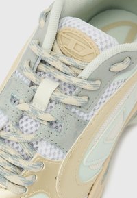 Vaalean beige ja vaaleansininen lenkkarit, joissa on verkkokangasta, mokkanahkaiset yksityiskohdat, kuvioidut nauhat ja beige soikea logo kielekkeessä.