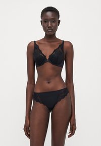 Reggiseno in pizzo nero con stecche e mutandine abbinate con bordo in pizzo nero. Il design presenta bordi scallop e una finitura liscia.