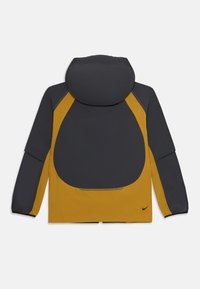 Crna i gorušičasta žuta Nike jakna s kapuljačom, dugim rukavima i malim crnim Nike logom na donjoj desnoj strani leđa.