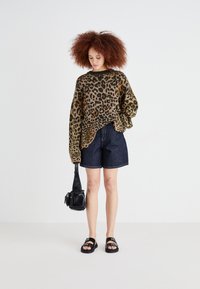 Pull en tricot imprimé léopard marron et noir, coupe oversized, assorti à un short en denim foncé, des sandales noires et un petit sac à main noir.