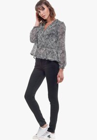 Blusa de estampado en blanco y negro con mangas acampanadas, tejido texturizado y bajo con volantes, combinada con jeans skinny negros y zapatillas blancas.