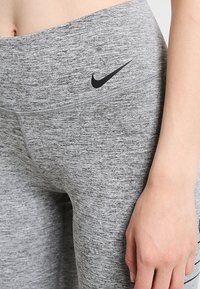 Szare legginsy z heatherowym wzorem o gładkiej fakturze, z czarnym logo Nike w pobliżu pasa i dopasowanym kroju.