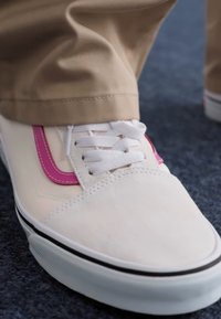 Hvide sneakers med lyserøde sideaccenter, snørebåndsdesign, gummisål og glat tekstur, sat sammen med khakibukser.