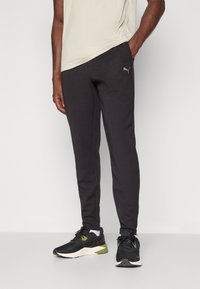 Zwarte sportbroek van zacht materiaal, met een slanke pasvorm, zijzakken en een klein grijs logo op de dij. G gedragen met zwarte sneakers.