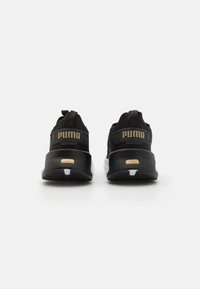 Sorte sportsko med strukturert overflate, med en tykk hvit såle og gullaccenter på hælen, merket med "PUMA."