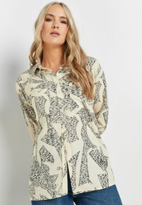 Long-sleeve button-up shirt in cream with a black abstract pattern; features a collar and a straight cut, made from a soft fabric.