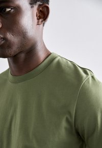 Olivengrønn crew-neck t-skjorte i myk, glatt stoff med korte ermer og avslappet passform, med et rent, minimalistisk design.