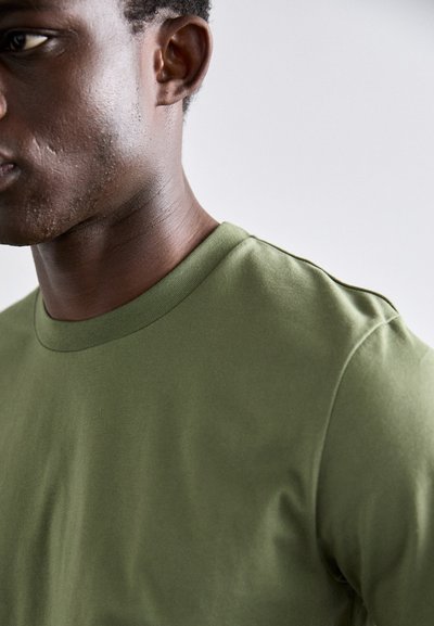 Oliivivärinen crew-neck T-paita pehmeästä ja sileästä kankaasta, jossa on lyhyet hihat ja rento istuvuus, ja joka esittelee puhtaan, minimalistisen muotoilun.