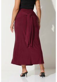 Burgundy maxikjol med en knuten midjedetalj, tillverkad av mjuk väv. Har en flödande siluett och slits i sidan för enkel rörelse.