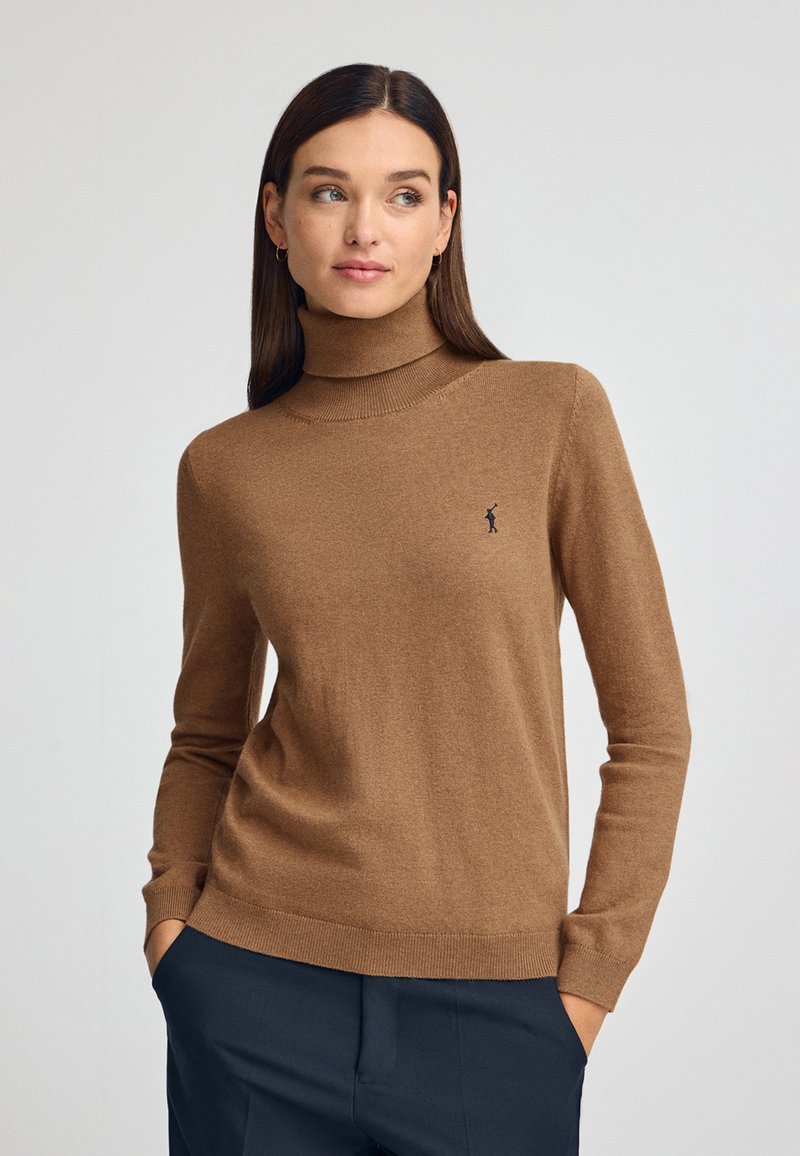 Pull à col roulé marron en tissu doux, avec des manches longues et une coupe ajustée. Comprend un petit logo sur la poitrine.