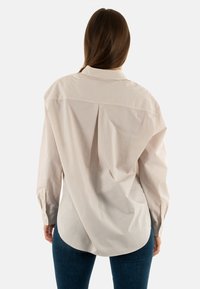 Camisa ligera a rayas en beige y crema, con yugo trasero, hombros caídos y puños abotonados. Con hem redondeado y corte holgado.