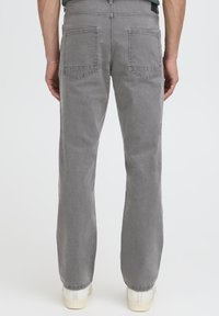 Jeans in denim grigio con design a gamba dritta, caratterizzati da due tasche posteriori, una texture liscia e un orlo pulito. Indossati con sneakers di colore chiaro.