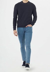 Marineblauer Pullover mit Rundhalsausschnitt und langen Ärmeln, kombiniert mit hellblauen Skinny-Jeans und dunklen Sneaker. Einfaches, klares Design mit lässigem Aussehen.