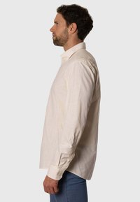 Camisa de lino beige claro de manga larga, con cuello clásico, puños abotonados y un diseño de corte relajado.