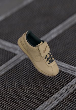 Beżowe skórzane sneakersy z zielonym wnętrzem, czarnymi sznurowadłami i paskiem z logo. Gładka tekstura i niskoprofilowy design.