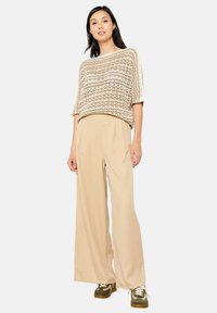 Cremfarbener und beiger Stricktop mit lockeren, kurzen Ärmeln, kombiniert mit hochtaillierten, weit geschnittenen beigen Hosen und grünen Sneakern.