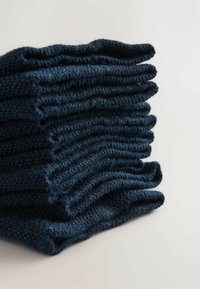 Stapel von ordentlich gefalteten dunkelblauen Strickpullovern auf einer hellen Oberfläche.