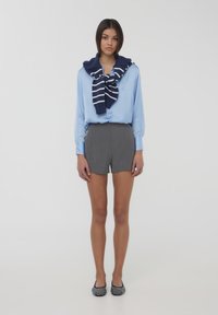 Camicia button-up azzurro chiaro abbinata a pantaloni corti grigi. Un maglione a righe blu navy annodato attorno alle spalle. Ballerine a fantasia bianco e nero completano il look.