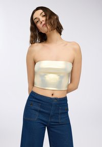 Metaliczny złoty top bez ramiączek w zestawieniu z niebieskimi dżinsami o wysokim stanie, posiadającymi dwie przednie kieszenie i kontrastowe szwy.