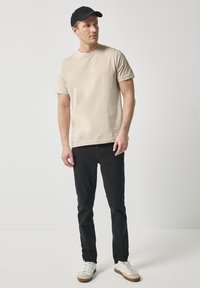 Béžové bavlněné tričko, krátké rukávy, kulatý výstřih, v kombinaci s černými slim-fit kalhotami a bílými teniskami s hnědými akcenty. Černá kšiltovka.