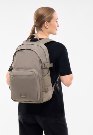 Kaki ryggsäck med vadderade axelremmar, framfickan med dragkedja och sidfickor i nät. Tyget har en slät yta och en minimalistisk design.