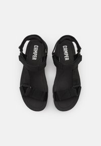 Sandalias negras con suela plana, correas ajustables y plantilla acolchada. El material superior es nylon con un acabado texturizado.