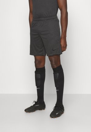Pantalones cortos deportivos negros hechos de una tela ligera con una cintura elástica, combinados con calcetines negros y zapatos de fútbol negros con acentos naranjas.