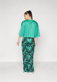 Haut vert court avec des manches courtes et trois rayures blanches. Pantalons amples à motifs dans des nuances de vert avec un design floral noir.