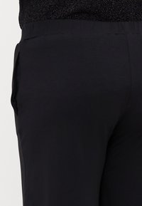 Black pants made of lightweight fabric with a smooth texture. Features a flat waistband and side pockets, visible at an angled view.
