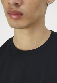 Tricou din bumbac negru cu guler rotund, având o textură netedă și un design minimalist, expus în zona gulerului.