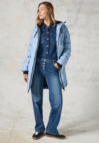 Ljusblå puffjacka med dragkedja och svarta detaljer, tillsammans med en denimoverall med knappar och vida denimbyxor.