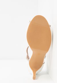 Chaussure à talons hauts blanche avec un empeigne lisse, un bout pointu et une semelle en caoutchouc couleur tan avec texture. Taille indiquée comme 37 sur la semelle.