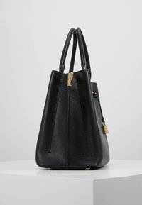 Czarna skórzana torebka o teksturowanym wykończeniu, kanciastym kształcie, złotych akcentach, z górnymi uchwytami i odpinanym zamkiem dekoracyjnym.